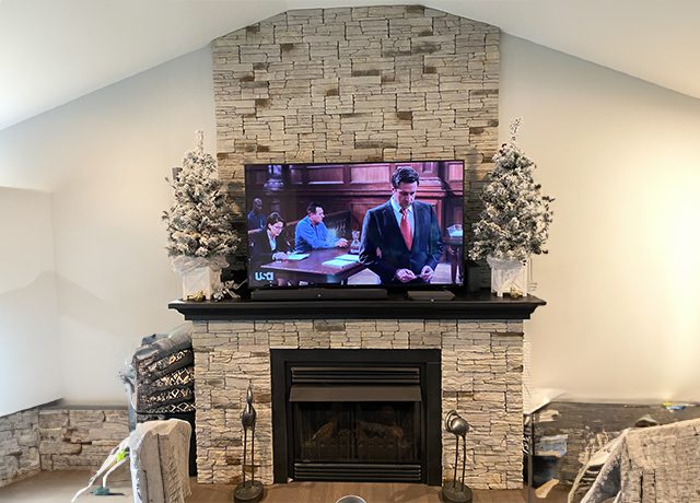 Stone fireplace with TV and plants.